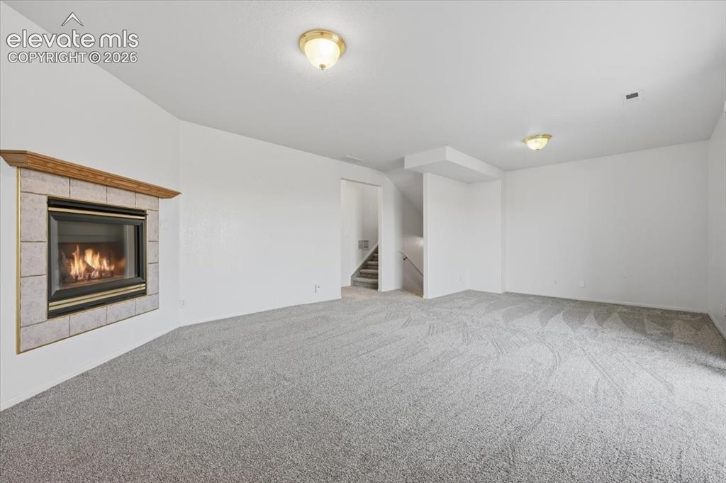Image 26 of 46: Recessed fireplace with tile surround, wood mantel, neutral carpet, and two