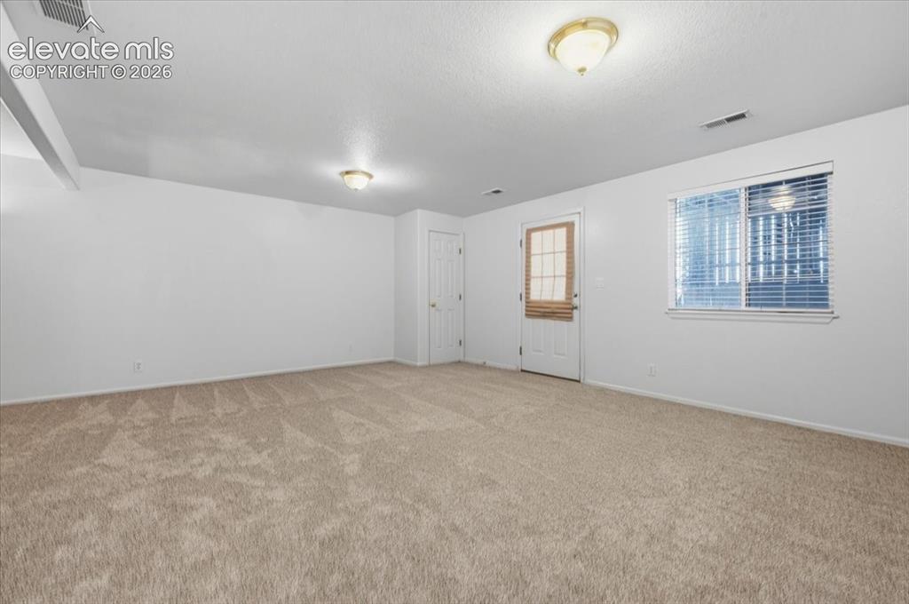 Image 31 of 46: Spacious room featuring neutral carpeting, a white door, a window with blin