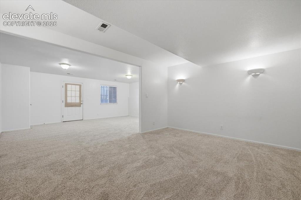 Image 35 of 46: Expansive carpeted area with recessed lighting, wall sconces, and a window 