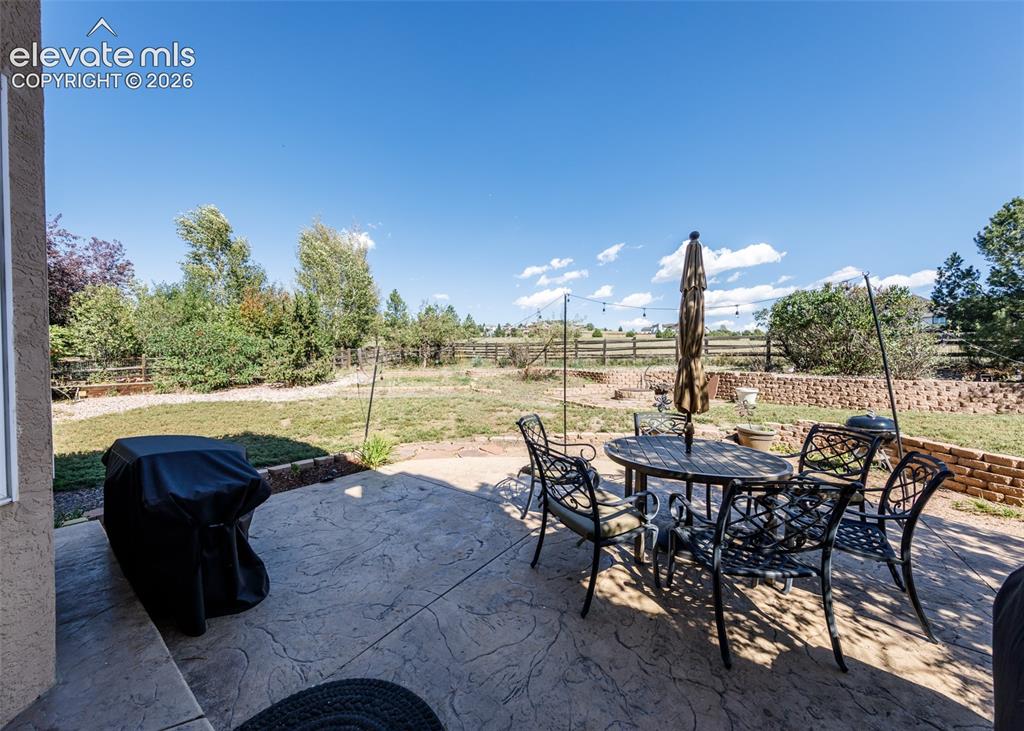 Image 37 of 38: Stamped concrete patio with a brick retaining wall and mature perimeter lan