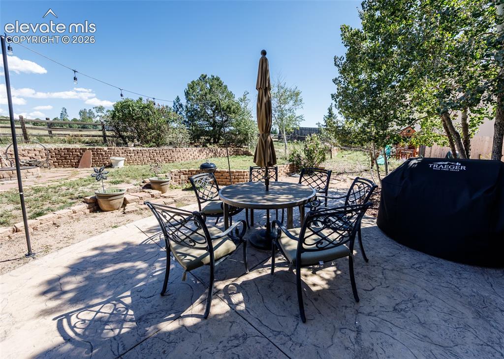 Image 38 of 38: Stamped concrete patio with a tiered retaining wall, string lighting, and m