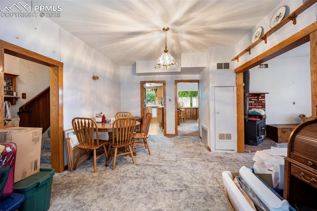 Image 12 of 48: Dining room with carpet, a wood stove, and a chandelier
