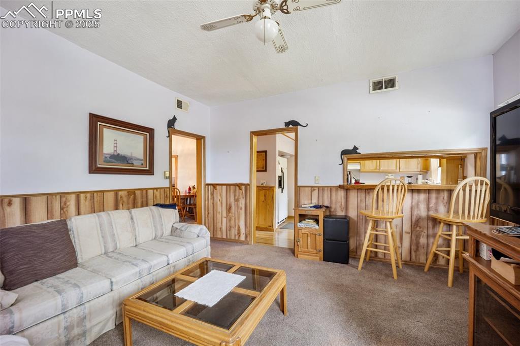 Image 15 of 48: Living area featuring ceiling fan, a wainscoted wall, wood walls, carpet, a