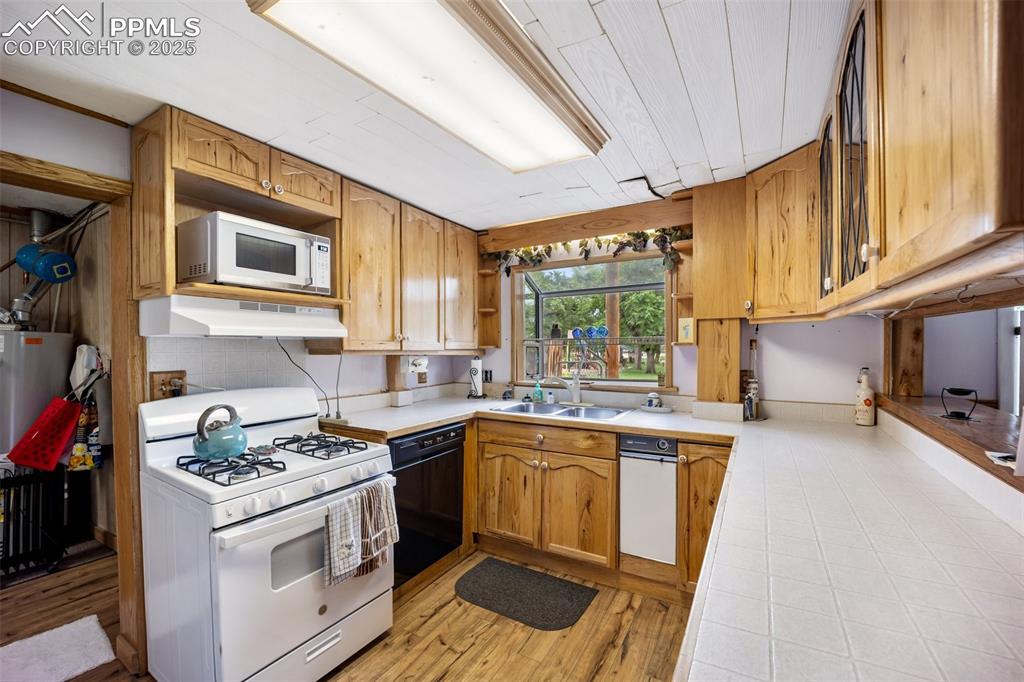 Image 16 of 48: Kitchen featuring white appliances, under cabinet range hood, open shelves,