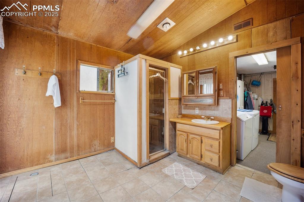 Image 22 of 48: Bathroom featuring vaulted ceiling, separate washer and dryer, wood walls, 