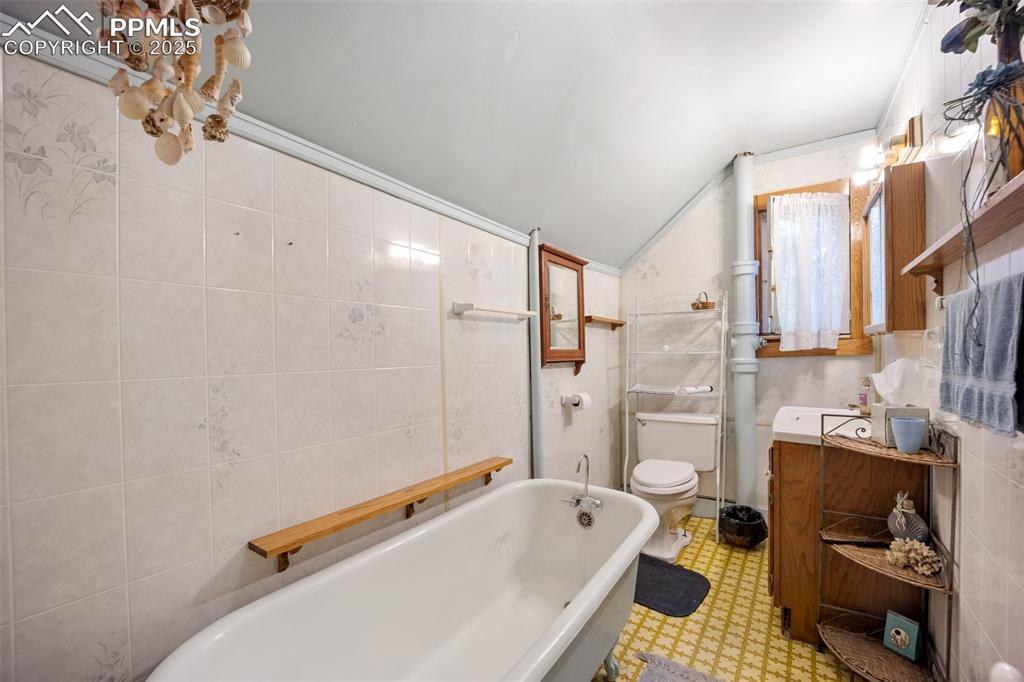Image 24 of 48: Bathroom with a bath, tile walls, lofted ceiling, tile patterned floors, an