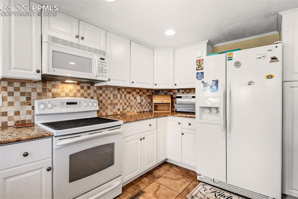 Image 10 of 38: Kitchen with granite counter tops, matching white cabinetry and appliances,