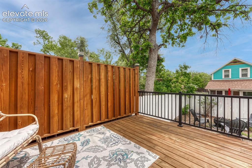 Image 14 of 21: Spacious wood-decked patio featuring a privacy fence and black metal railin