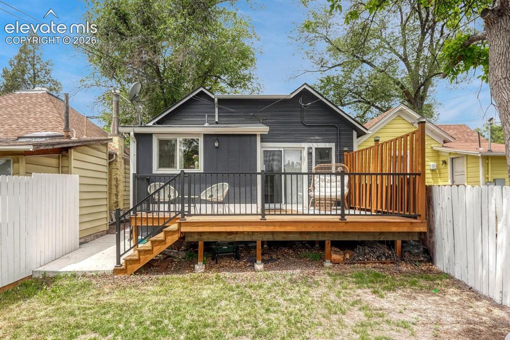 Image 18 of 21: Rear exterior featuring a wood deck with black metal railings, wood privacy