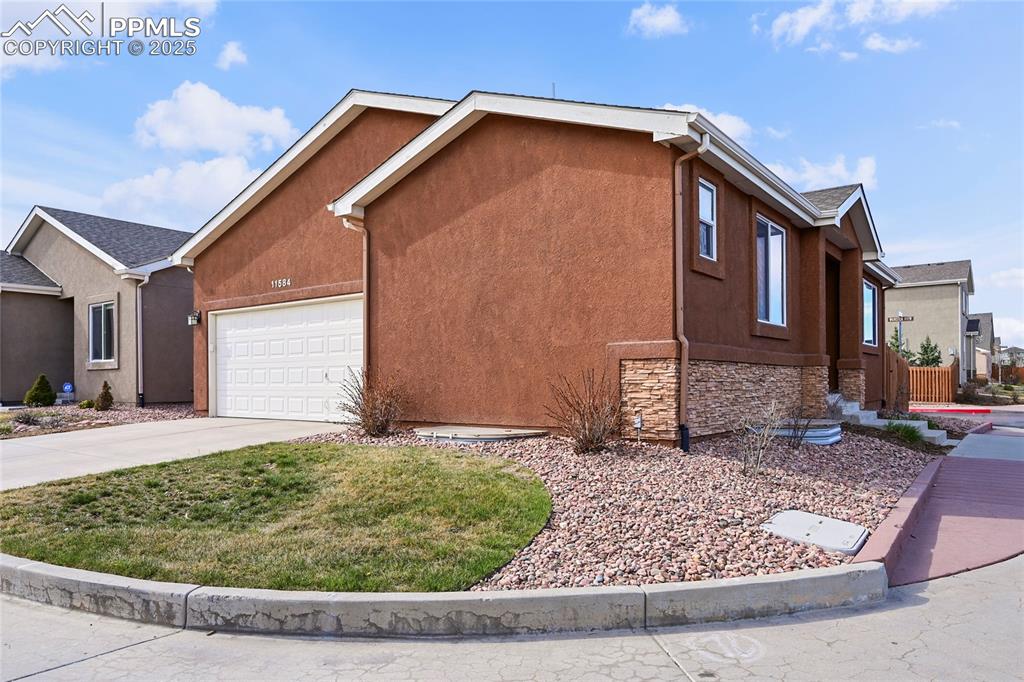 Caption: View of property exterior featuring stucco siding, driveway, stone siding, and a garage