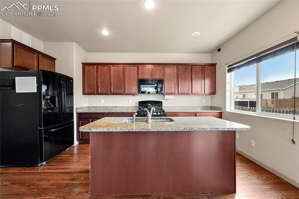 Image 6 of 22: Kitchen featuring black appliances, dark wood-style flooring, light stone c