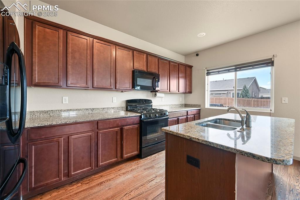 Image 9 of 22: Kitchen with black appliances, light stone counters, a sink, and light wood