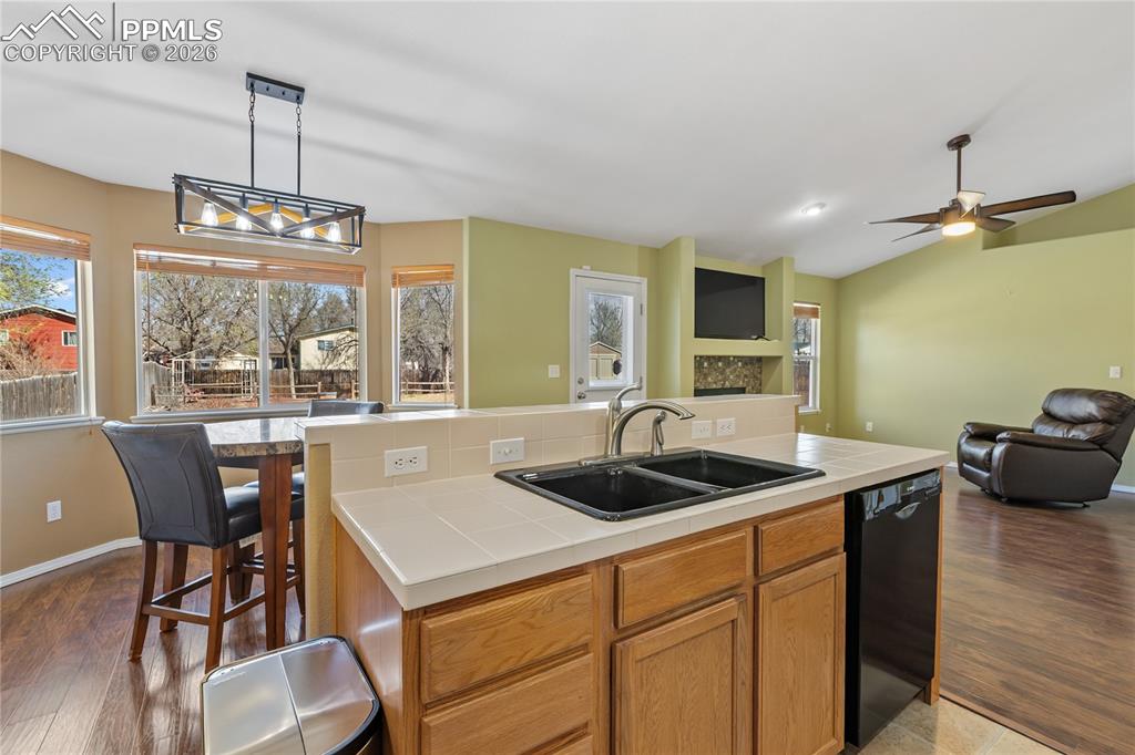 Image 17 of 36: Kitchen with tile countertops, an island with sink, dishwasher, open floor