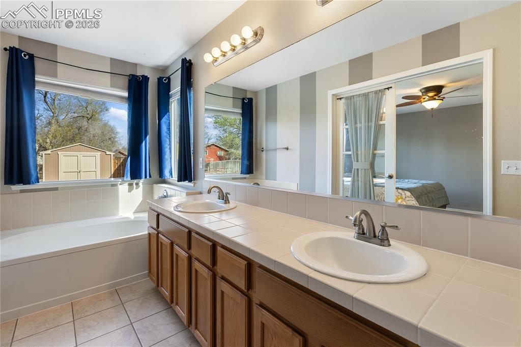 Image 22 of 36: Full bath with ensuite bathroom, double vanity, a bath, ceiling fan, and li