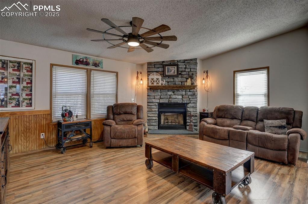 Image 16 of 31: Living room featuring a textured ceiling, a stone fireplace, wooden walls,