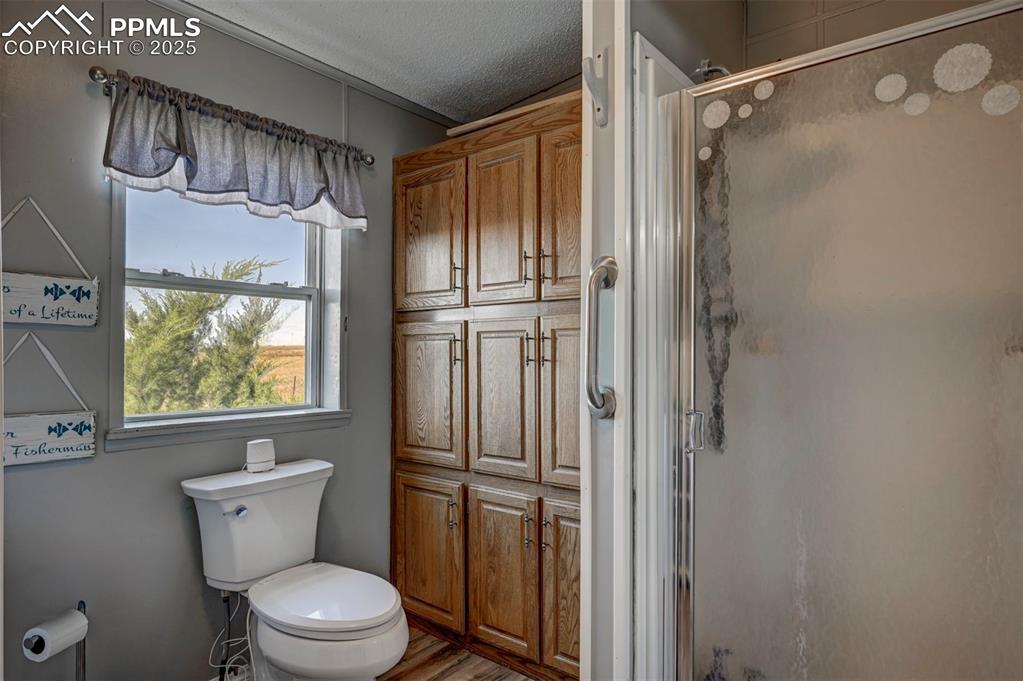 Image 24 of 31: Full bath featuring a textured ceiling, a shower stall, and wood finished f