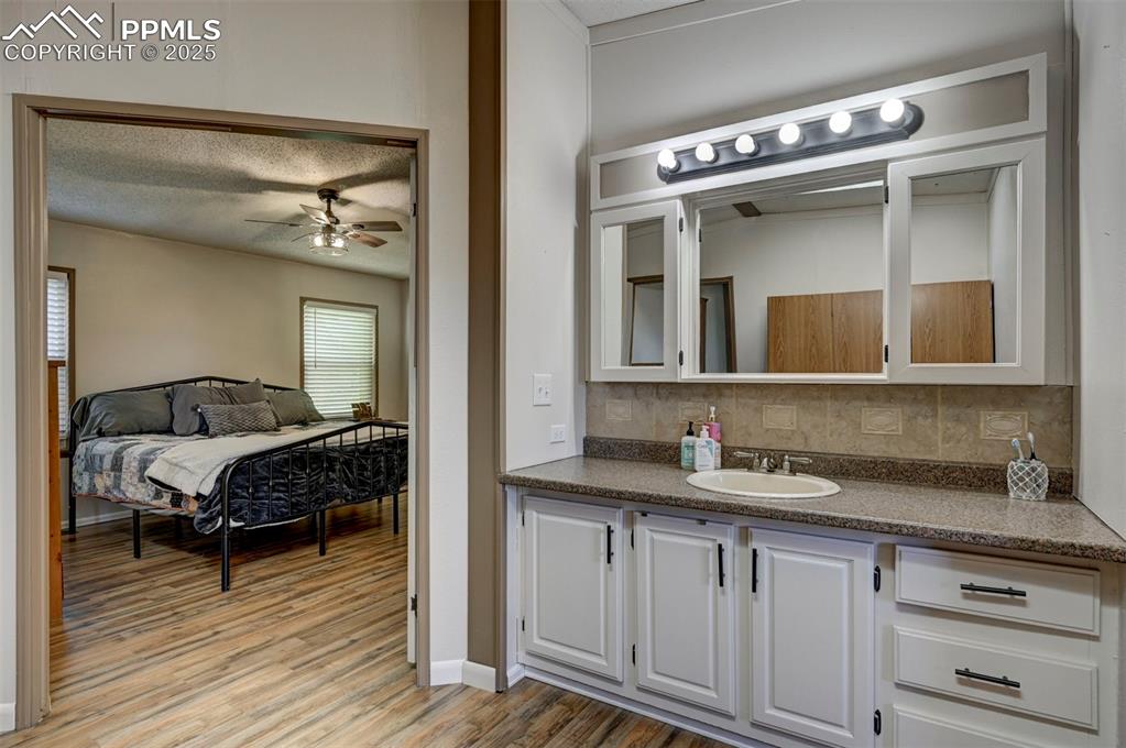 Image 25 of 31: Ensuite bathroom with a textured ceiling, vanity, backsplash, light wood-st