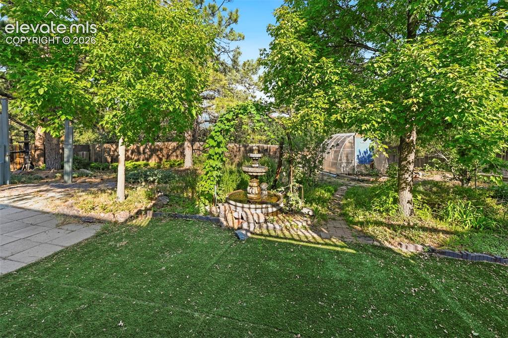 Image 32 of 43: Fenced yard featuring a stone-look tiered fountain, artificial turf, mature