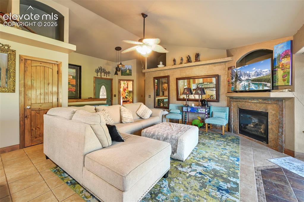 Image 5 of 43: Spacious living area featuring a corner fireplace with stone surround, tile