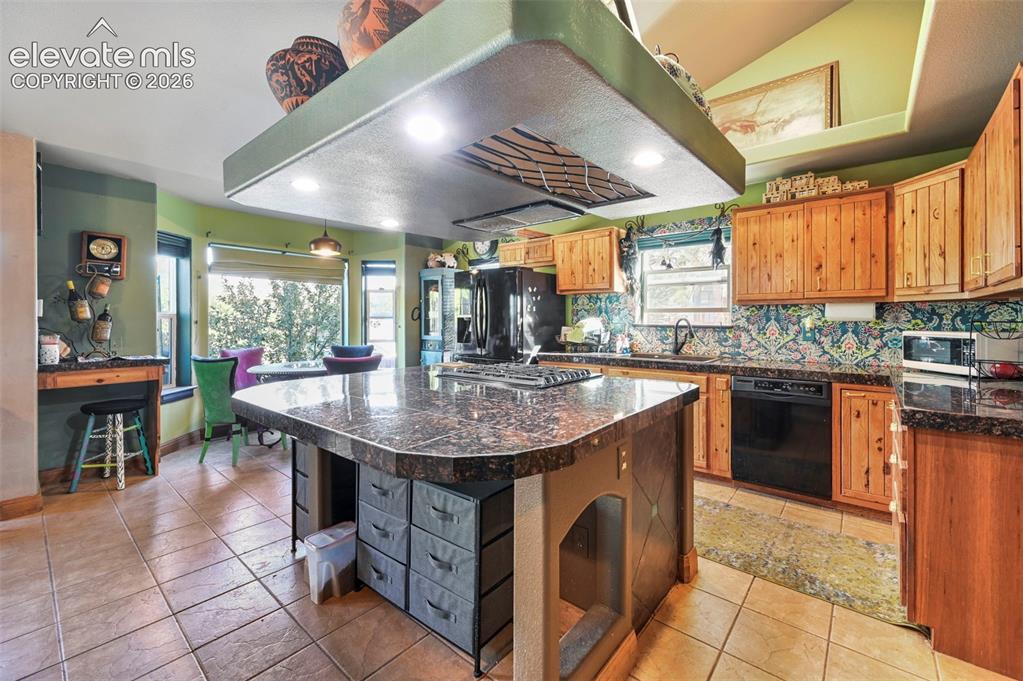 Image 7 of 43: Kitchen featuring a large central island with a dark stone countertop, an i