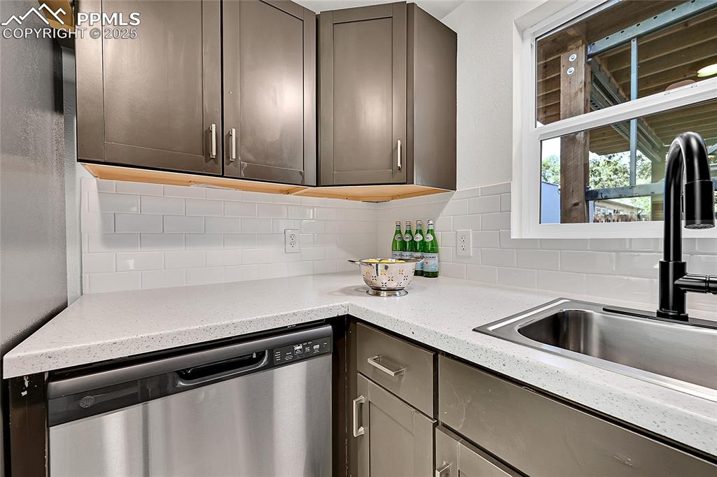 Image 13 of 30: Kitchen with dishwasher, light stone countertops, backsplash, and gray cabi