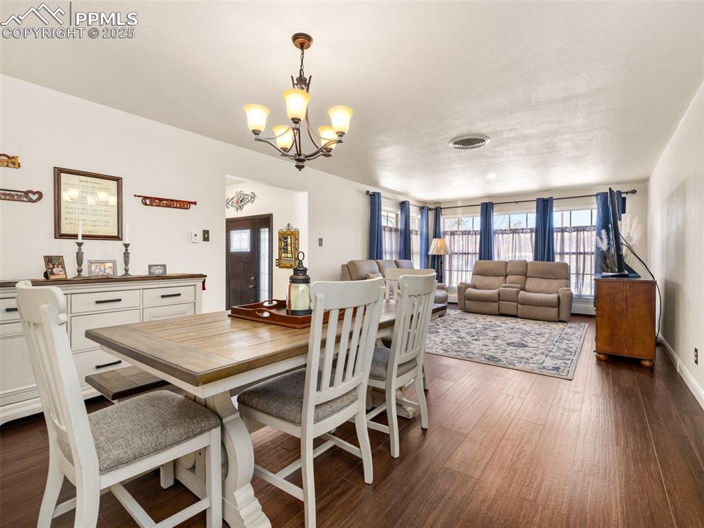 Image 12 of 41: Dining room with dark wood-style vinyl floors and a chandelier