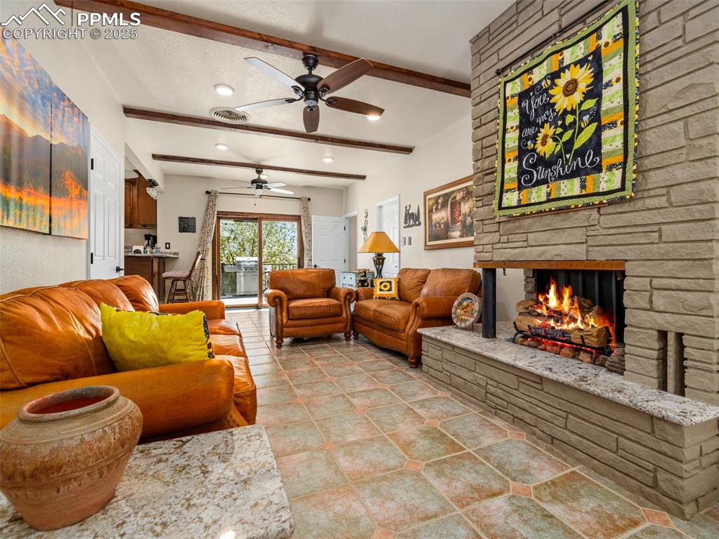Image 3 of 41: Living room featuring beam ceiling, a stone gas/log fireplace, a ceiling fa