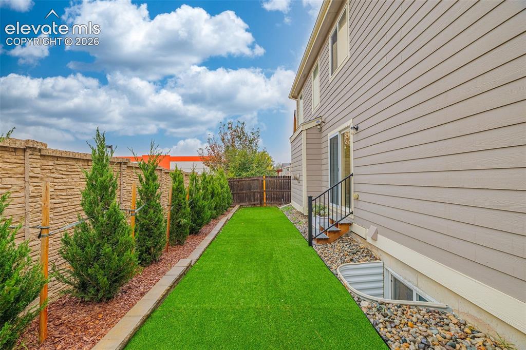 Image 31 of 35: Side yard featuring synthetic turf, structured evergreen plantings, decorat