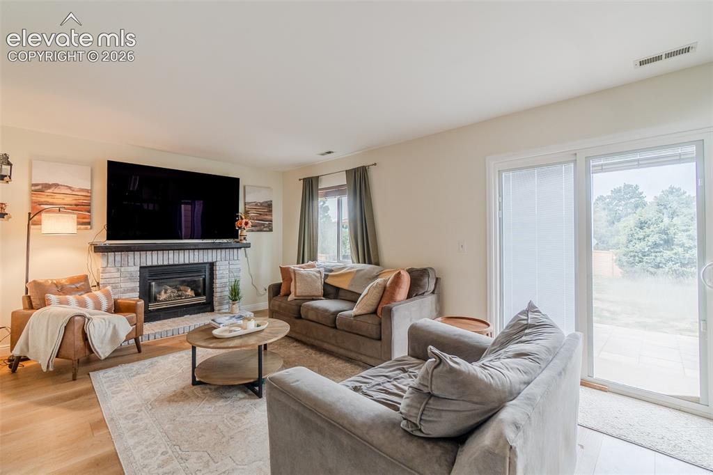 Image 10 of 31: Living area featuring a stone-clad fireplace, wood-finish flooring, and sli
