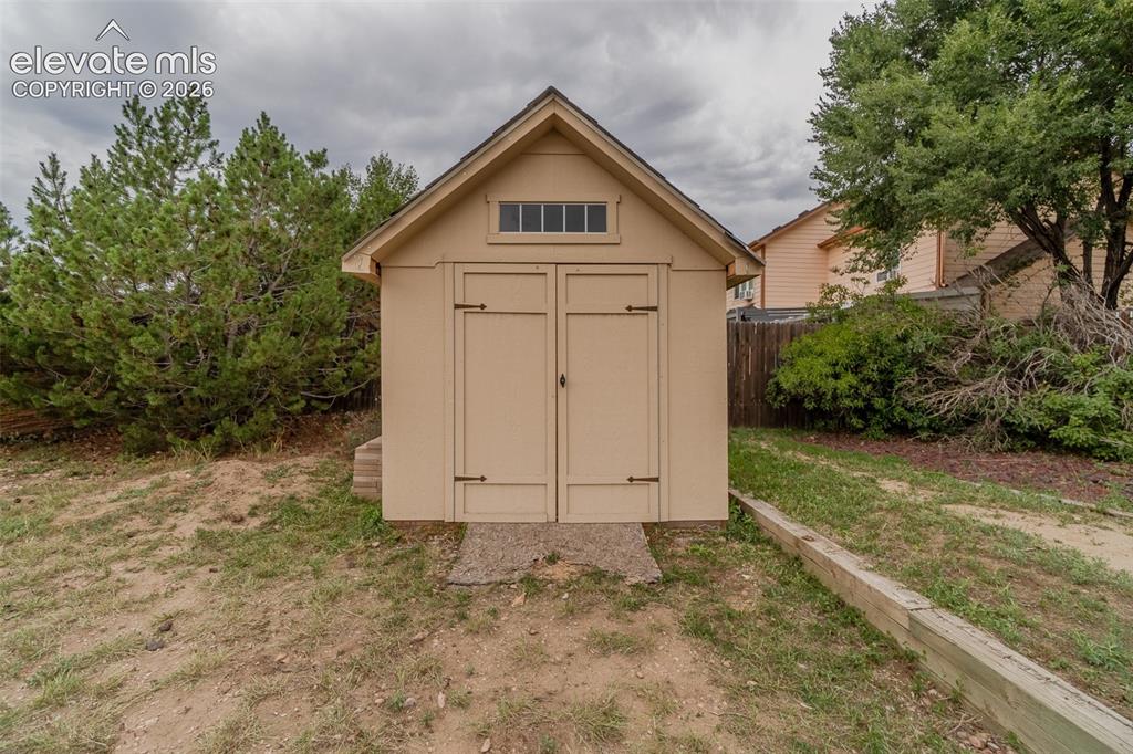 Image 23 of 31: Gable-roof storage shed featuring louvered transom windows and hinged doubl