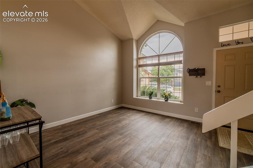 Image 3 of 31: Vaulted ceiling with an arched window, wood-finish flooring, and a paneled