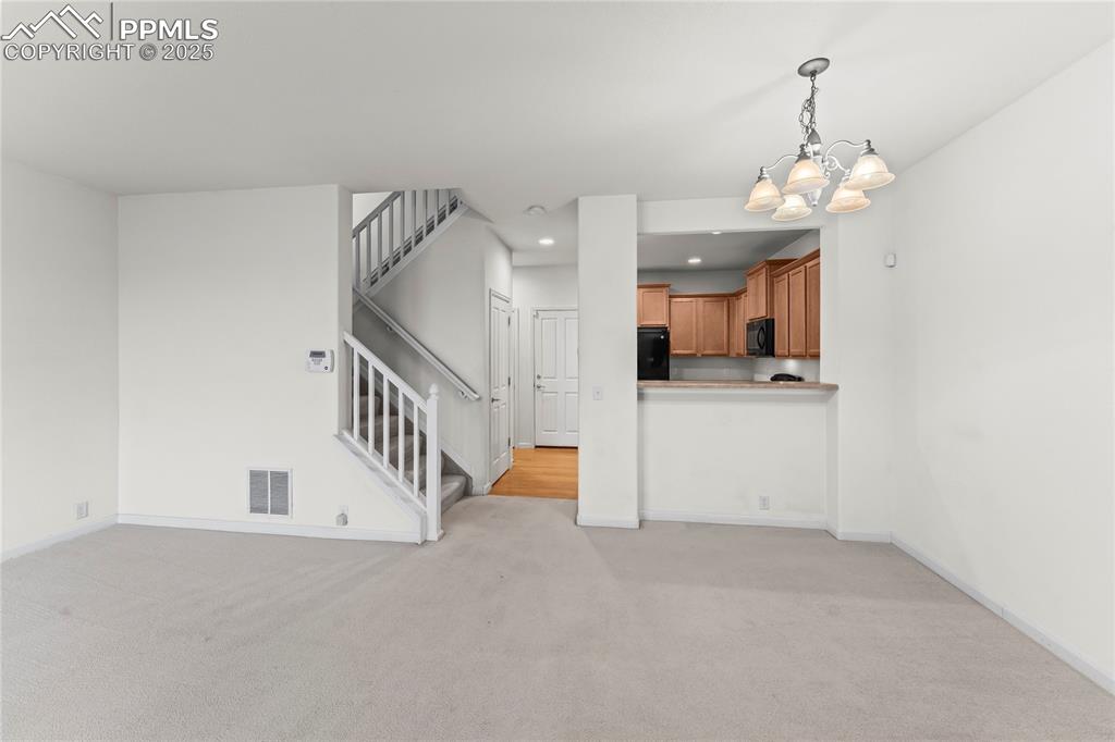 Image 6 of 26: Unfurnished living room with light colored carpet, stairway, a chandelier, 