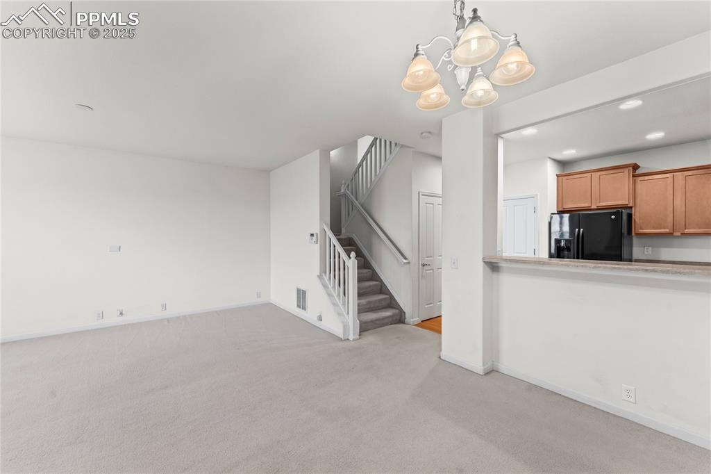 Image 9 of 26: Unfurnished living room featuring a chandelier, light colored carpet, stair