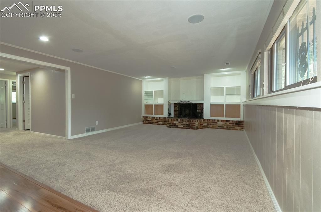 Image 17 of 42: Unfurnished living room featuring carpet flooring, crown molding, a brick f