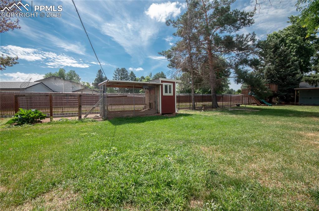 Image 31 of 42: Fenced backyard with a playground, an outdoor structure, and exterior struc
