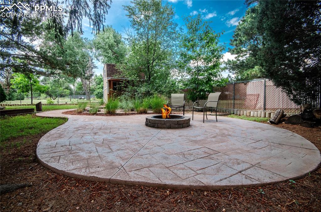 Image 34 of 42: View of patio with a fire pit, an outbuilding, and view of scattered trees