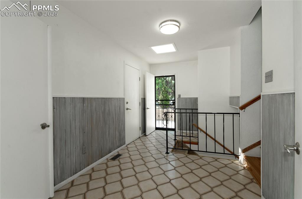 Image 6 of 42: Corridor featuring tile patterned floors, an upstairs landing, wooden walls