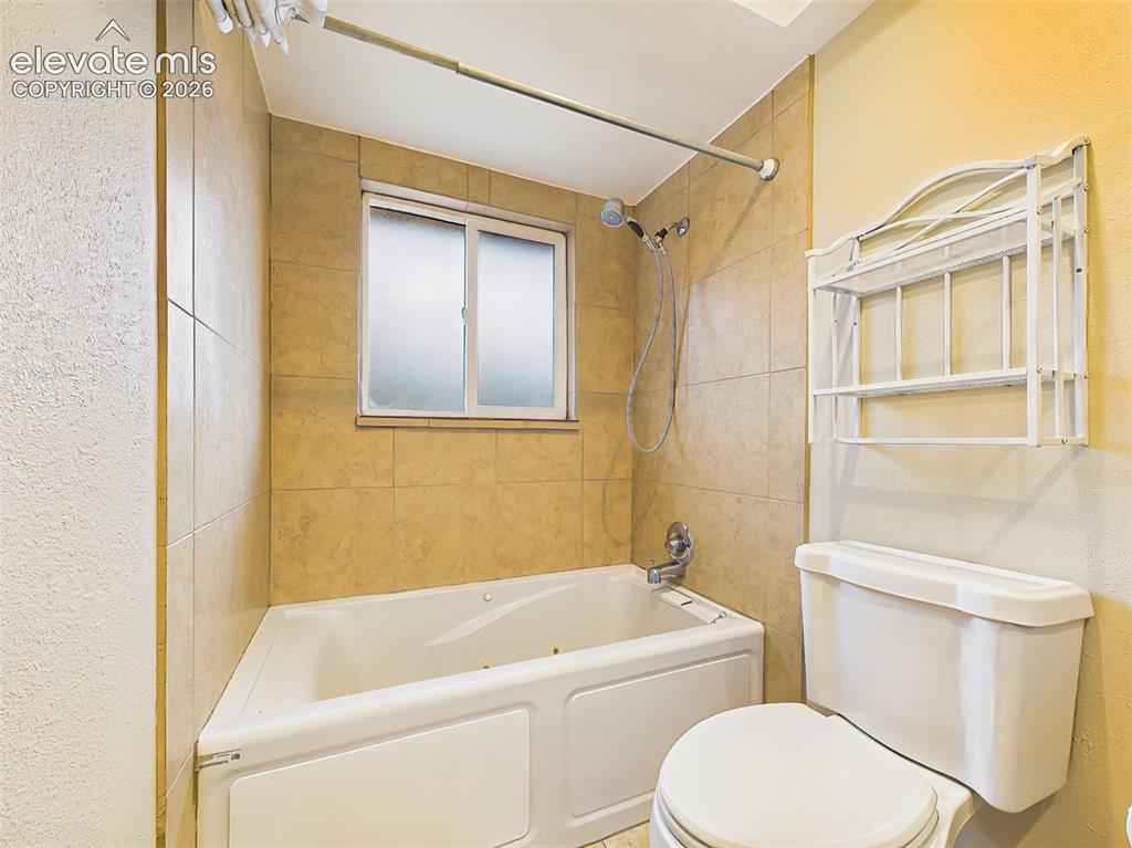 Image 28 of 50: Tiled tub and shower surround with built-in shelving and a frosted window f
