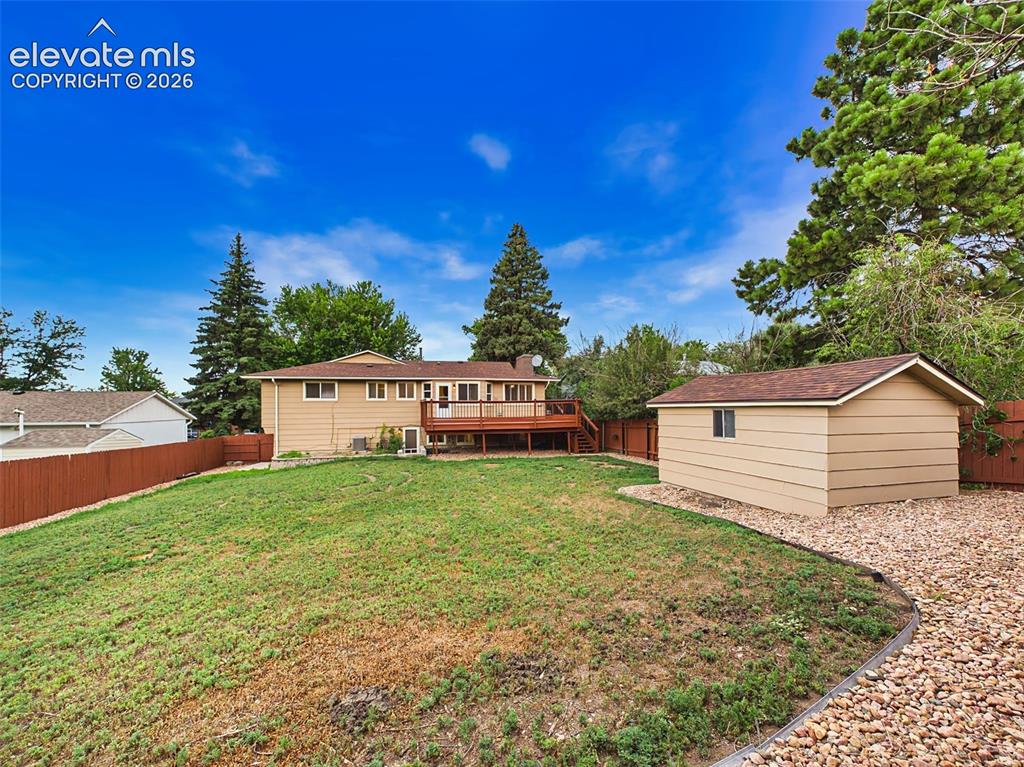Image 43 of 50: Expansive, fully fenced backyard with a large lawn, mature trees, and a spa