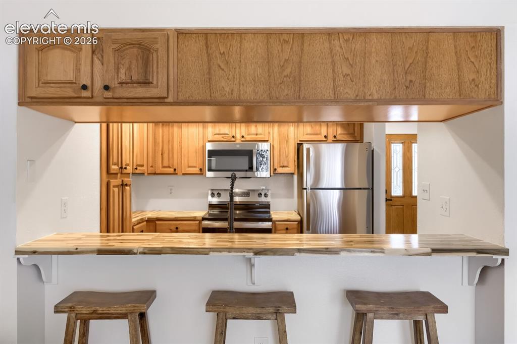 Image 10 of 25: Kitchen featuring a wood-finish breakfast bar, light wood cabinetry, stainl