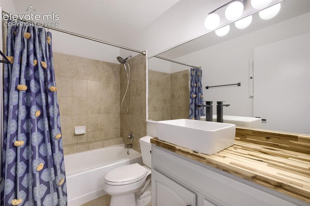 Image 14 of 25: Bathroom featuring a white rectangular vessel sink, wood-finish countertop,