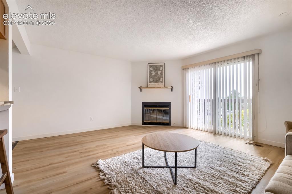 Image 5 of 25: Living area featuring wood-finish flooring, a corner fireplace with a black