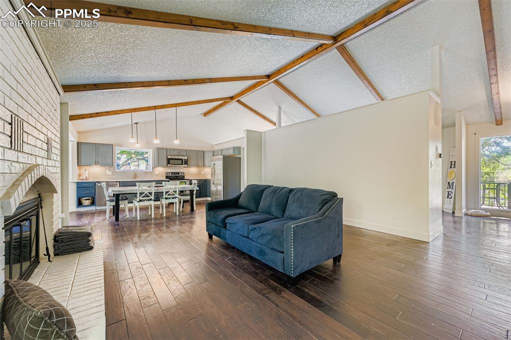 Image 12 of 37: Living room featuring a textured ceiling, beam ceiling, a brick fireplace,