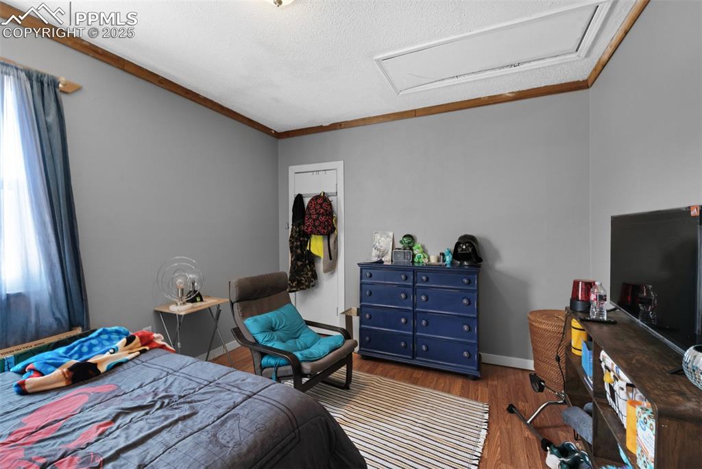 Image 18 of 26: Bedroom featuring attic access, wood finished floors, baseboards, and ornam