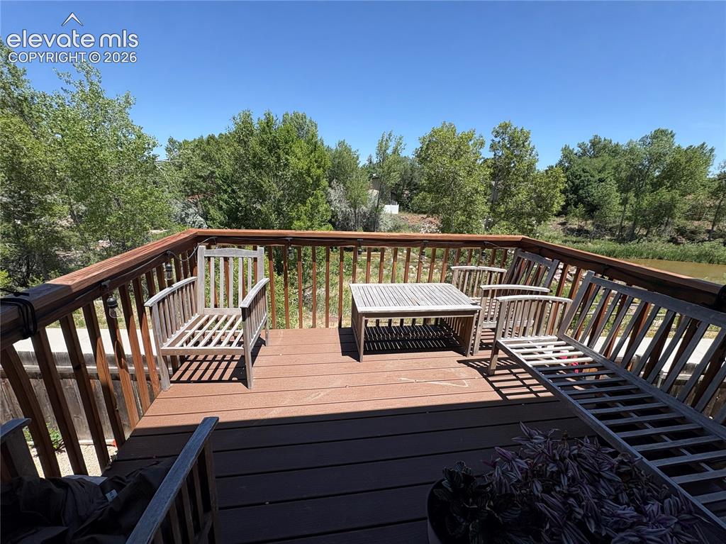 Image 11 of 11: Outdoor wood-finish deck with wood railing, overlooking mature trees and a