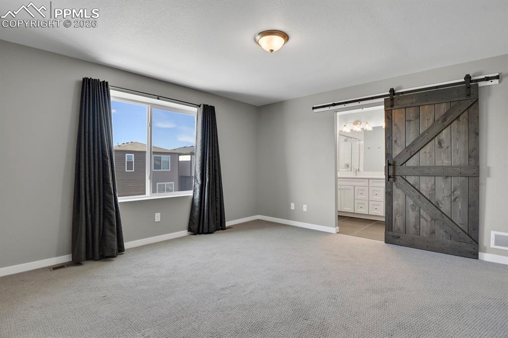Image 20 of 40: Unfurnished bedroom featuring a barn door, light colored carpet, and connec