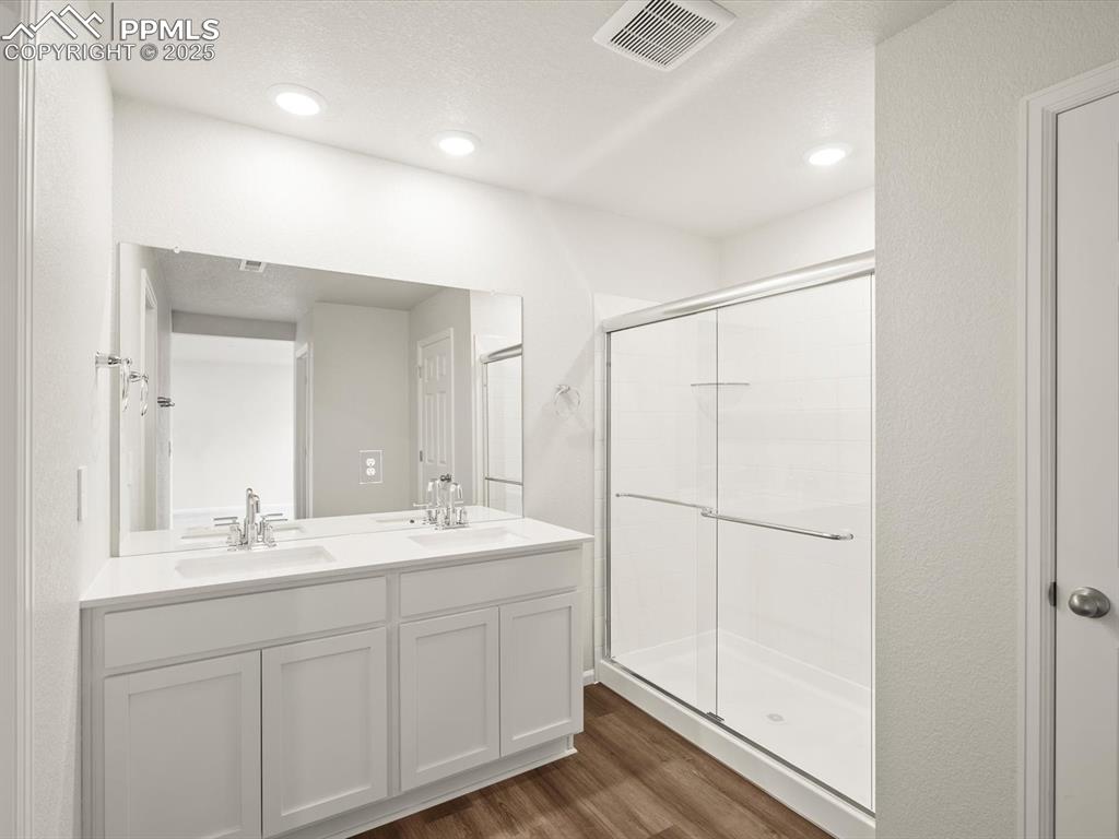 Image 14 of 23: Bathroom featuring a shower stall, wood finished floors, double vanity, and