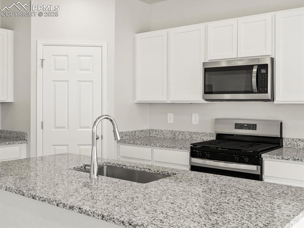 Image 3 of 23: Kitchen with stainless steel appliances, white cabinetry, and light stone c