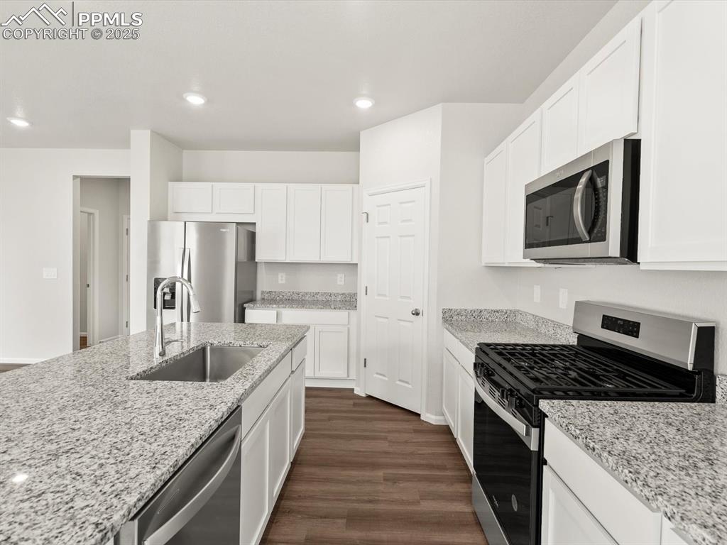 Image 4 of 23: Kitchen with stainless steel appliances, dark wood-style flooring, white ca