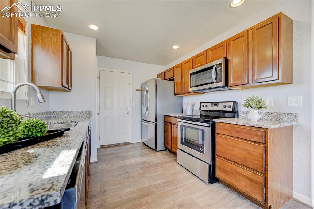 Image 10 of 37: Kitchen with brown cabinets, light wood-style flooring, a sink, recessed li